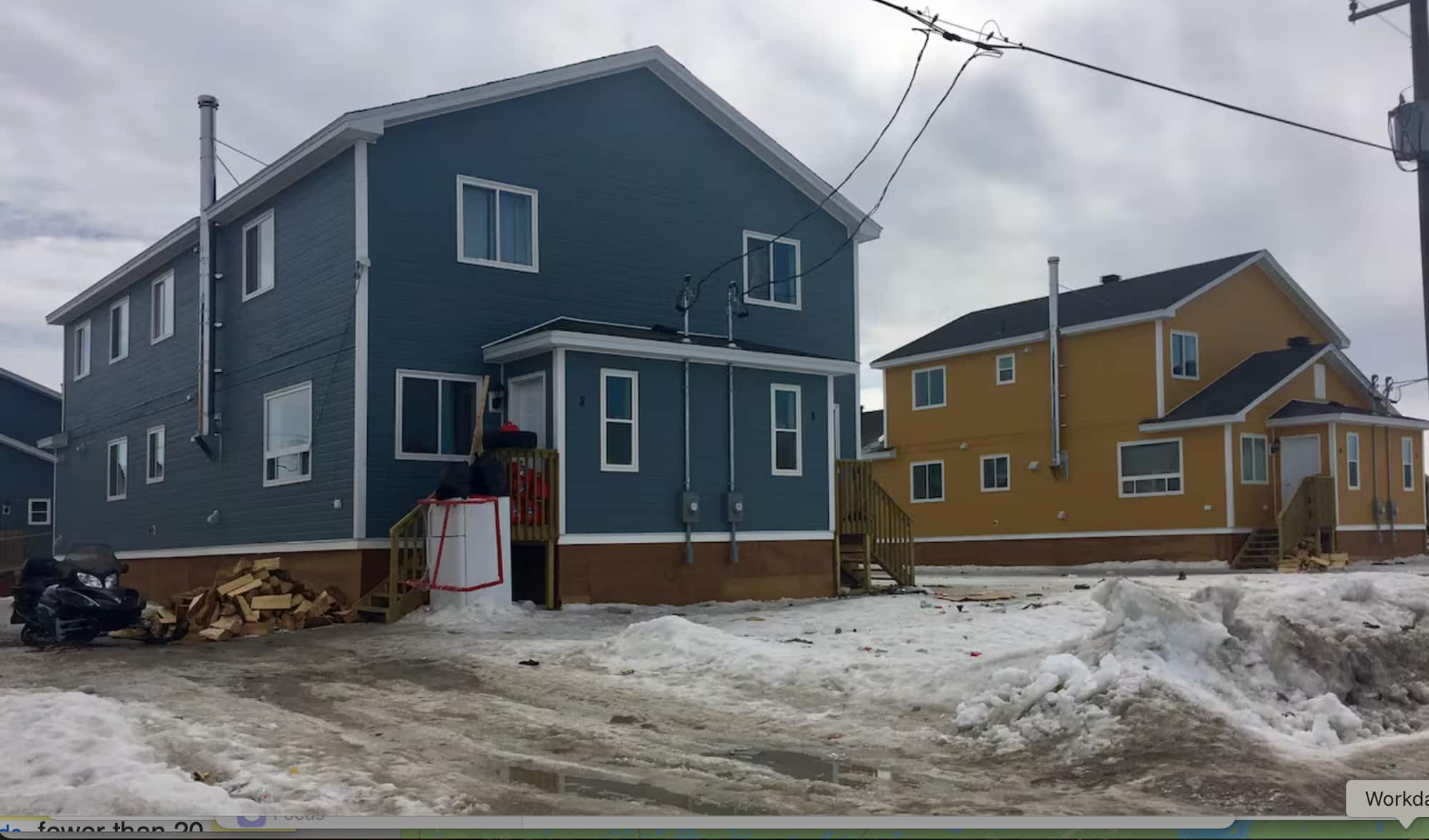 A two-storey blue house is next to a yellow one on snowy ground. 